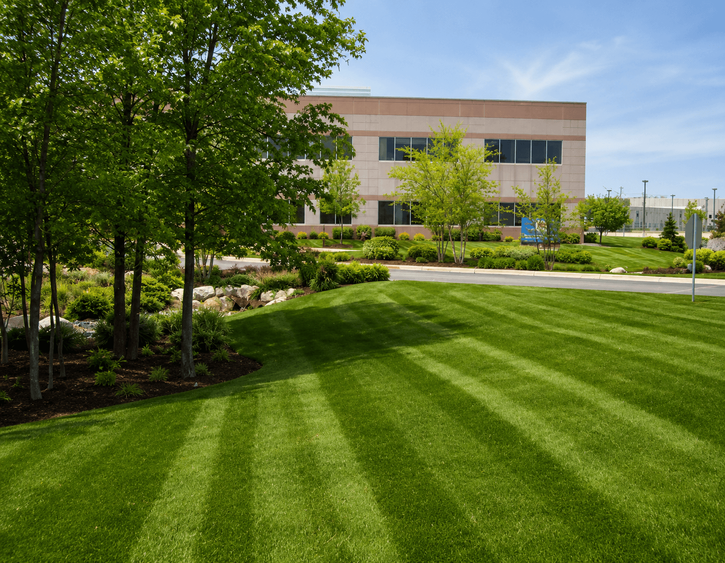 Manicured striped lawn and lush landscaping in front of a modern commercial office building.