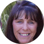 Smiling woman with dark brown hair and bangs, blue eyes, in a circular profile picture.