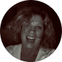 Circular sepia-toned headshot of a woman with curly hair laughing with a wide, joyful smile.